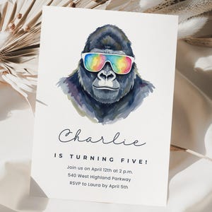 May include: A birthday invitation featuring a watercolor illustration of a gorilla wearing rainbow sunglasses. The text reads "Charlie is turning five!" with event details below. The invitation is on a white background.