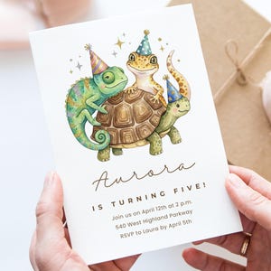 Könnte beinhalten: Eine Aquarell-Geburtstagseinladung mit einem Chamäleon, einem Gecko und einer Schildkröte mit Partyhüten. Die Einladung lautet "Aurora wird fünf!" mit Veranstaltungsdetails. Die Einladung wird von einer Person gehalten.