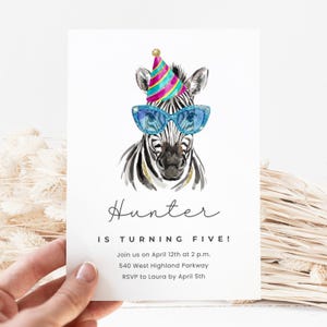 Op de afbeelding: Witte uitnodigingskaart met een illustratie van een zebra met zonnebril en een feesthoed. De tekst luidt "Hunter wordt vijf!" met evenementdetails. Een hand houdt de kaart vast.