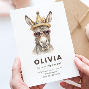 Puede incluir: Una invitación de cumpleaños con una ilustración en acuarela de un burro con gafas de sol en forma de corazón, un gorro de fiesta y una pajarita. La invitación dice "¡OLIVIA cumple siete años!" con los detalles del evento.