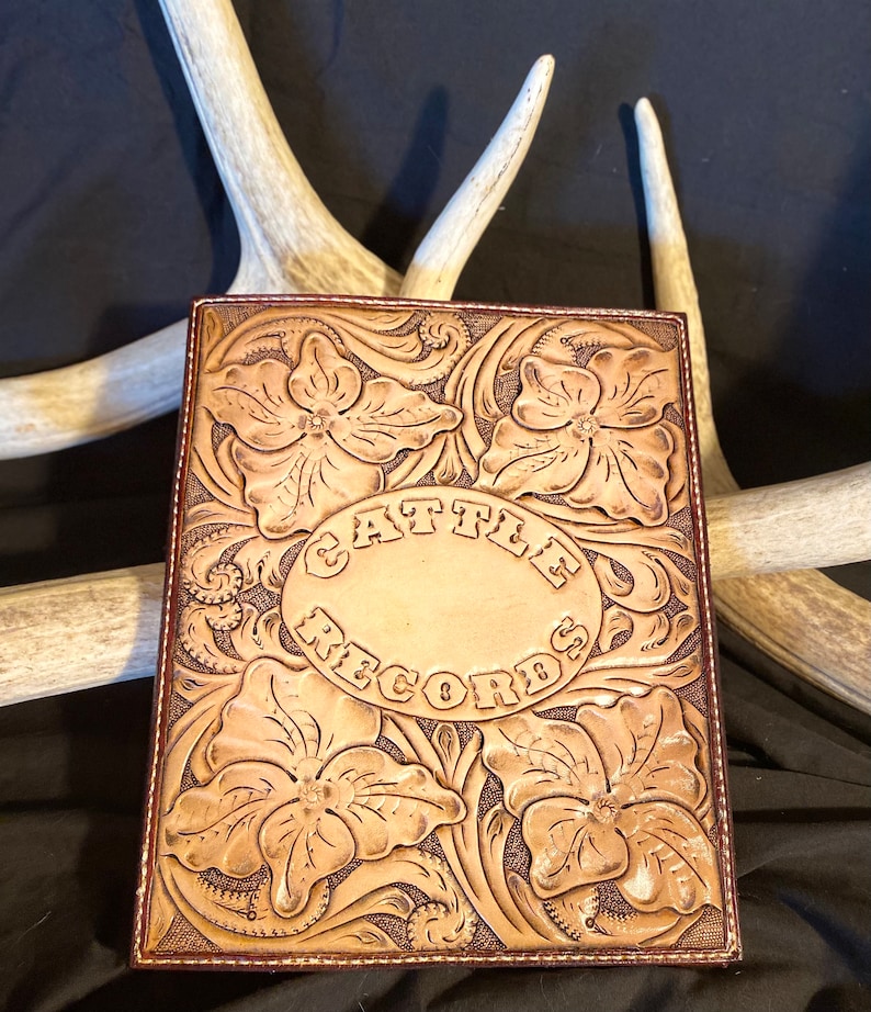 Puede incluir: Un diario de cuero marr&oacute;n con dise&ntilde;os florales tallados y las palabras "Cattle Records" en relieve en el centro.