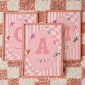Puede incluir: Tres cuadros rectangulares con fondo de cuadros y rayas rosas. Cada lámina muestra una letra grande en el centro dentro de un óvalo festoneado, rodeada de pequeños corazones, estrellas y dibujos de flores de colores.
