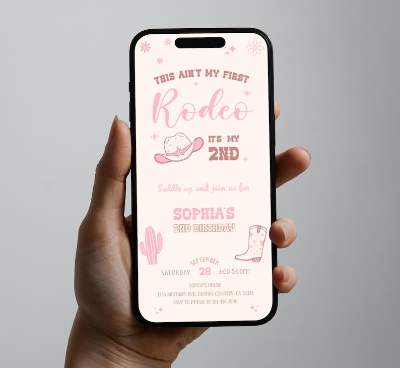 K&ouml;nnte beinhalten: Ein Smartphone zeigt eine digitale, rosafarbene Geburtstagseinladung mit dem Text This Aint My First Rodeo It's My 2nd, verziert mit einem Cowboyhut, einem Kaktus und einem Cowboystiefel sowie den Details f&uuml;r Sophias 2. Geburtstag.
