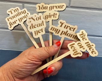 May include: Six wooden plant stakes with humorous sayings, including "I'm rooting for you", "Not dead yet", "You grow girl!" and "I wet my plants".