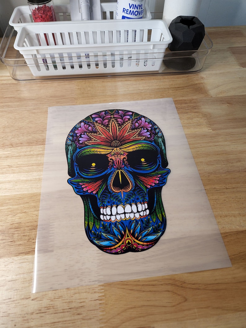 May include: A colorful skull with floral designs in shades of blue, red, yellow, and green. The skull is outlined in black and has a detailed design.