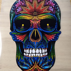 May include: A colorful sugar skull with intricate floral designs and a marijuana leaf on the forehead. The skull is blue, green, red, yellow, and orange.