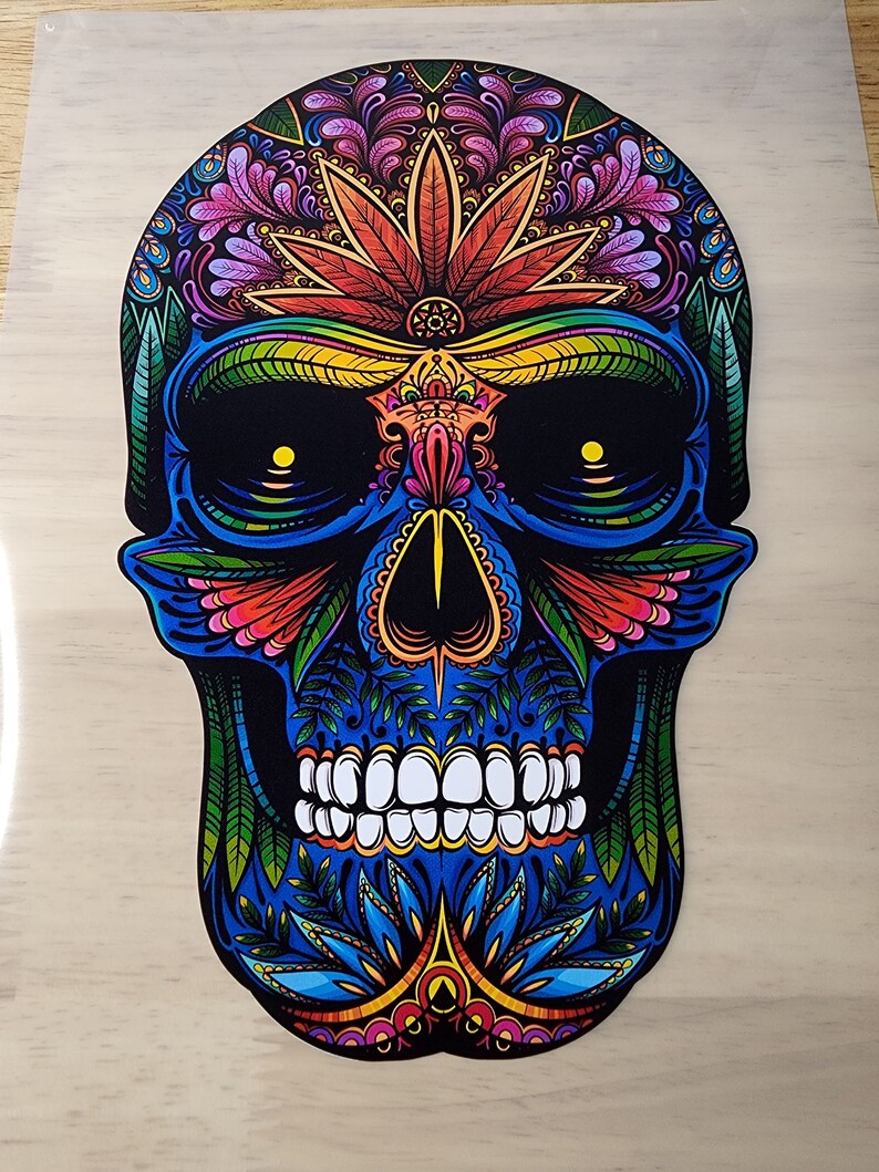 May include: A colorful sugar skull with intricate floral designs and a marijuana leaf on the forehead. The skull is blue, green, red, yellow, and orange.