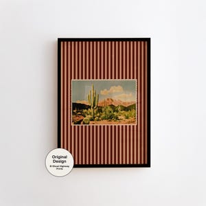 May include: Framed art print depicting a desert scene with cacti and mountains. The artwork is set against a backdrop of vertical red and pink stripes. The frame is black, and the print includes the text "Original Design" and "Ghost Highway Prints."