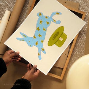 Folk art style blue bunny wall print with gold stars and olive green top hat, hand drawn in oil pastel on cream — whimsical printable wall decor.