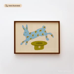 Hand illustrated printable wall art of a blue star-covered rabbit leaping over a green magician's hat on a cream background, shown framed in dark wood — instant digital download.