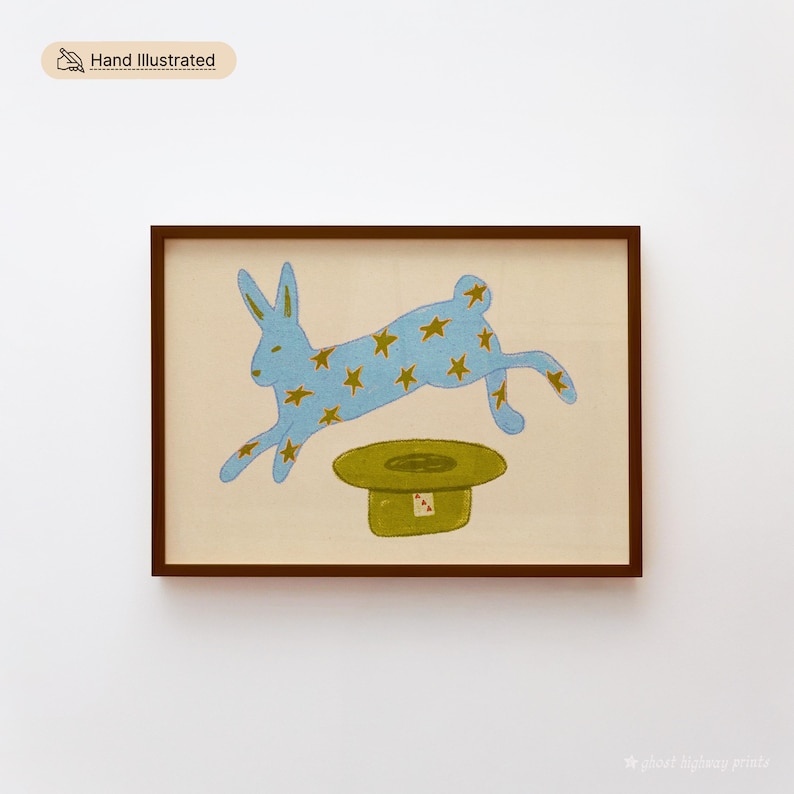 Hand illustrated printable wall art of a blue star-covered rabbit leaping over a green magician's hat on a cream background, shown framed in dark wood — instant digital download.