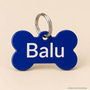 Könnte beinhalten: Eine knochenförmige Haustiermarke in leuchtendem Königsblau. Der Name Balu ist in klaren, fetten weißen Großbuchstaben in der Mitte der Marke aufgedruckt. Ein runder silberner Metallring ist zur Befestigung durch das obere Loch gezogen.