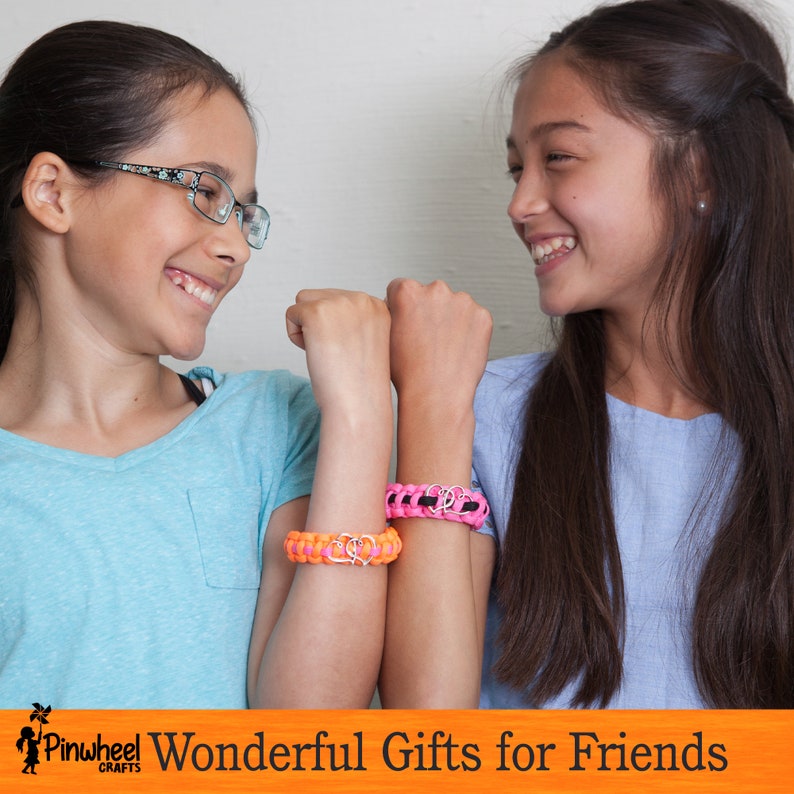 May include: Two friends wearing friendship bracelets with heart charms. The bracelets are made with colorful paracord and are a great gift idea for friends.