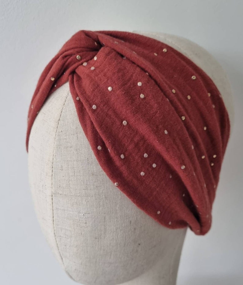 May include: A rust-colored turban headband with a gold polka dot pattern. The headband is made of a soft, stretchy fabric and is designed to be worn as a fashion accessory.