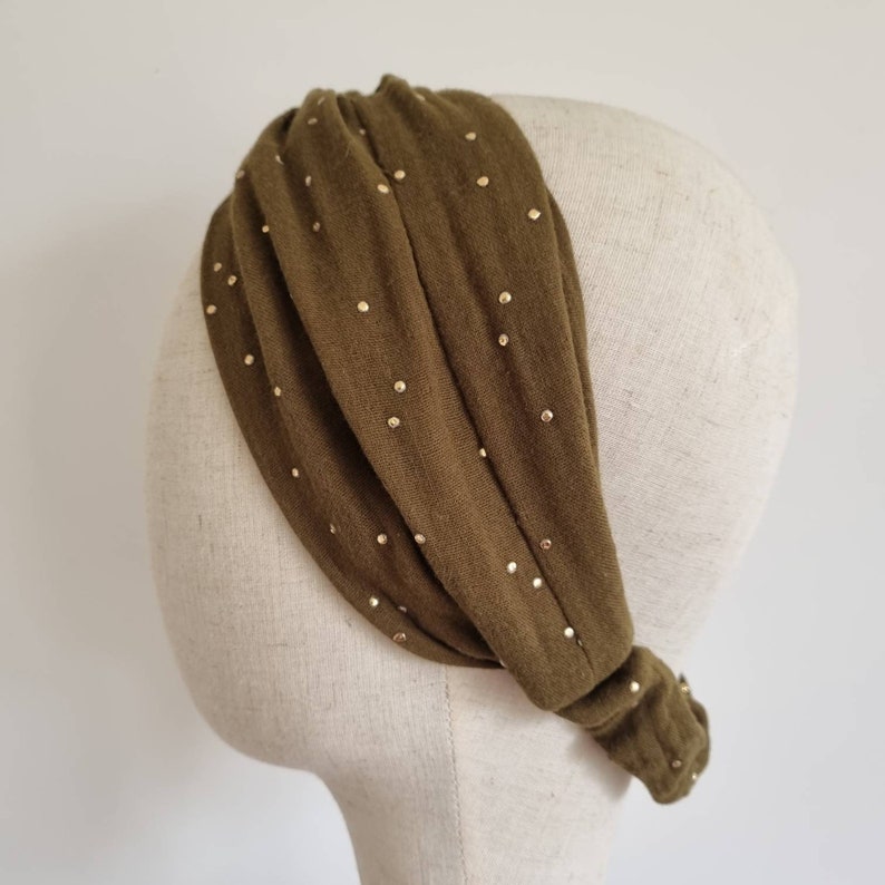 May include: A green headband with gold dots. The headband is made of a soft, stretchy fabric and is designed to be worn around the head.