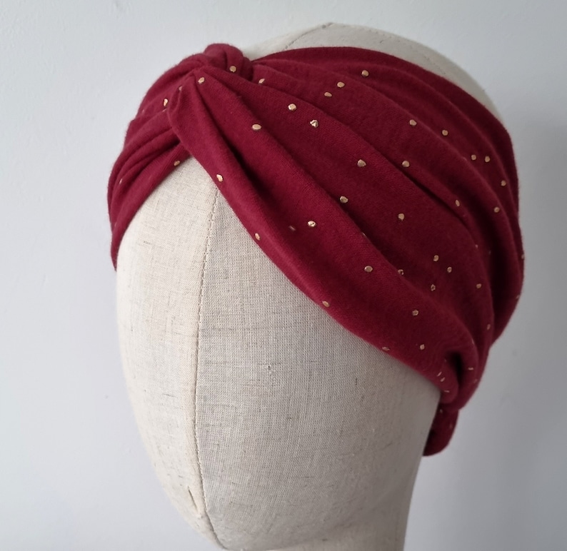 May include: A burgundy turban headband with gold polka dots. The headband is made of a soft, stretchy fabric and is designed to be worn as a fashion accessory.