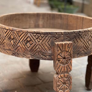 May include: A round wooden table with a carved design around the top edge. The table has three legs, each with a carved design.
