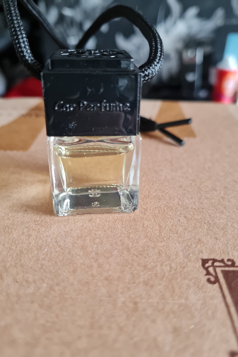 May include: A small, clear glass bottle with a black cap and a black label that says "Car Perfume". The bottle is hanging from a black string.
