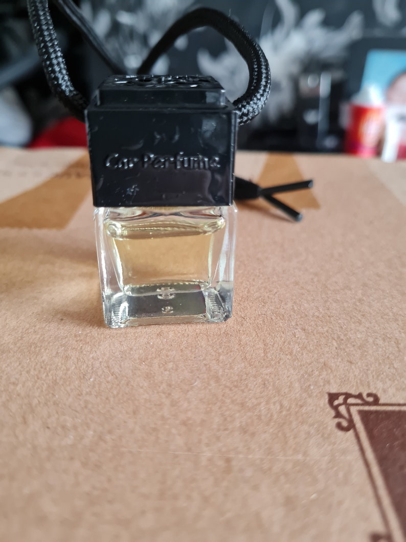 May include: A black and clear glass car air freshener with a black string hanging from the top. The air freshener has the text "Car Perfume" printed on the front.