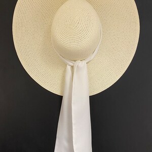 May include: A white straw sun hat with a wide brim and a white satin ribbon tied around the crown. The ribbon has the text "Mrs. Smith" embroidered on it.