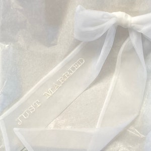 May include: White tulle ribbon with a bow and the text "Just Married" embroidered on it.