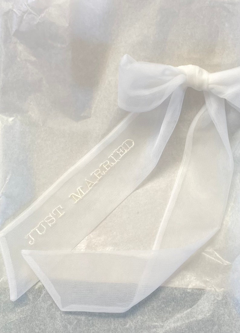 May include: White tulle ribbon with a bow and the text "Just Married" embroidered on it.