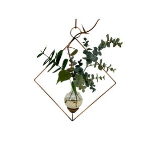 May include: A copper geometric hanging planter with a glass bulb vase containing greenery. The planter is in the shape of a diamond and has a simple, modern design.