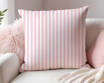 May include: A decorative pillow with vertical pink and white stripes sits on a white armchair. A pink pillow and a fluffy pink cushion are also on the chair. A white fringed throw blanket is draped over the arm of the chair.