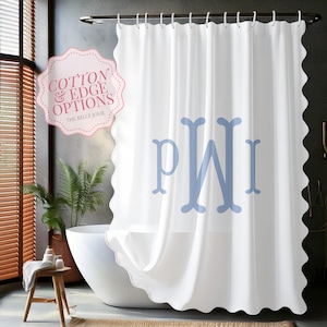 May include: A white shower curtain with a scalloped edge and a large light blue monogram featuring the letters PWI. A pink scalloped label in the upper left corner displays the text COTTON & EDGE OPTIONS THE BELLE JOLIE.