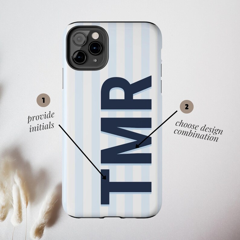 Może przedstawiać: Etui na telefon w biało-błękitne paski z granatowymi inicjałami "TMR". Etui posiada wycięcie na aparat oraz tekst "provide initials" i "choose design combination".
