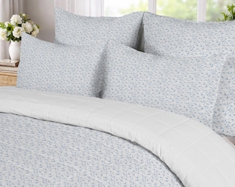 May include: A bedding set featuring a white quilt and matching pillow shams with a small-scale blue floral pattern. The quilt has a grid-like stitched texture, while the pillow shams display the same blue and white floral print.