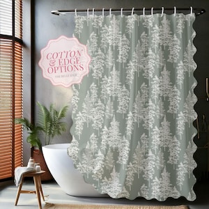 May include: A sage green shower curtain with a white pine tree pattern. The curtain has a scalloped edge and is hanging in a bathroom. The text "COTTON & EDGE OPTIONS" is visible on a pink label.