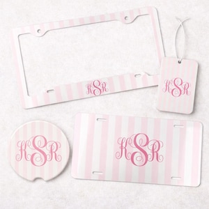 May include: A set of accessories featuring a light pink and white vertical striped pattern with the monogram KSR in pink script. The set includes a rectangular license plate frame, a rectangular license plate, a circular coaster, and a luggage tag.