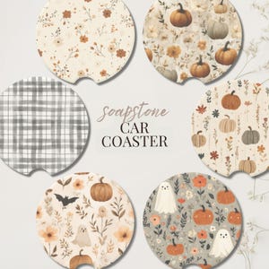 May include: A collection of soapstone car coasters with various fall-themed designs. The coasters feature pumpkins, floral patterns, and a plaid design. The text "soapstone CAR COASTER" is in the center.