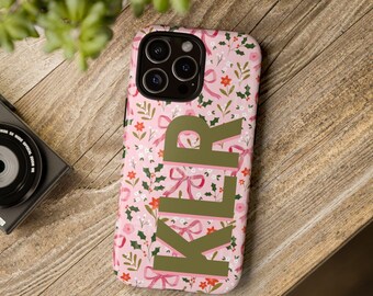 May include: A pink smartphone case featuring a repeating pattern of red flowers, green holly leaves, and pink ribbons. The letters KLR are printed in large, solid olive green block capitals vertically down the center of the phone case.