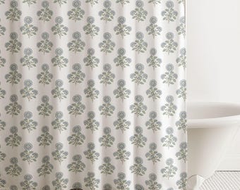 May include: A white shower curtain featuring a repeating pattern of blue floral motifs with green stems and leaves. The fabric is draped in vertical folds, displaying a consistent botanical design across the entire surface of the curtain.