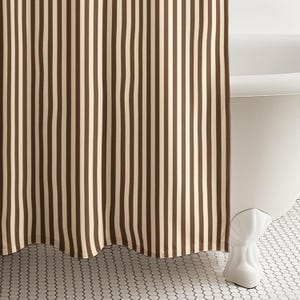 May include: A brown and cream striped shower curtain hangs in front of a white clawfoot bathtub. The curtain has vertical stripes and a scalloped bottom edge. The bathroom floor has a white and gray tile pattern.
