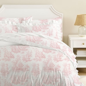 May include: White bed linens with a pink toile pattern featuring pastoral scenes. The bedding includes a duvet cover, pillowcases, and a ruffled edge. The headboard is white with a decorative trim.