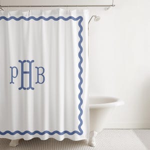 May include: A white shower curtain featuring a blue wavy border along the edges and a centered blue monogram with the letters PHB. The curtain hangs from a metal rod and is positioned in front of a white bathtub in a bathroom setting.