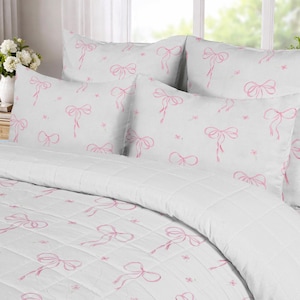 May include: A white bedding set featuring a repeating pattern of light pink hand-drawn style bows. The set includes a quilted coverlet and matching pillow shams, all decorated with the same delicate pink bow motif across the white fabric surface.