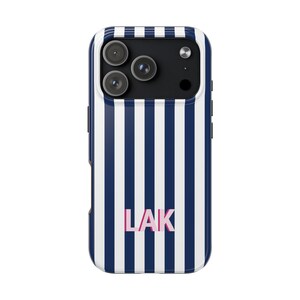 May include: A smartphone case featuring a vertical navy blue and white striped pattern. The back of the case displays the letters LAK in a light pink font centered near the bottom. The camera module area is black with three circular lenses.