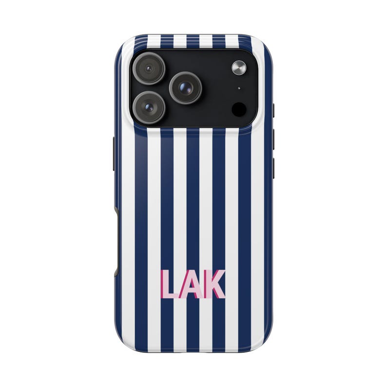 May include: A smartphone case featuring a vertical navy blue and white striped pattern. The back of the case displays the letters LAK in a light pink font centered near the bottom. The camera module area is black with three circular lenses.