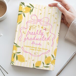 May include: A graduation-themed notebook with a lemon and ribbon design. The cover features the text "freshly graduated" in pink, along with a name, school, and class year. Yellow lemons and green leaves decorate the background.