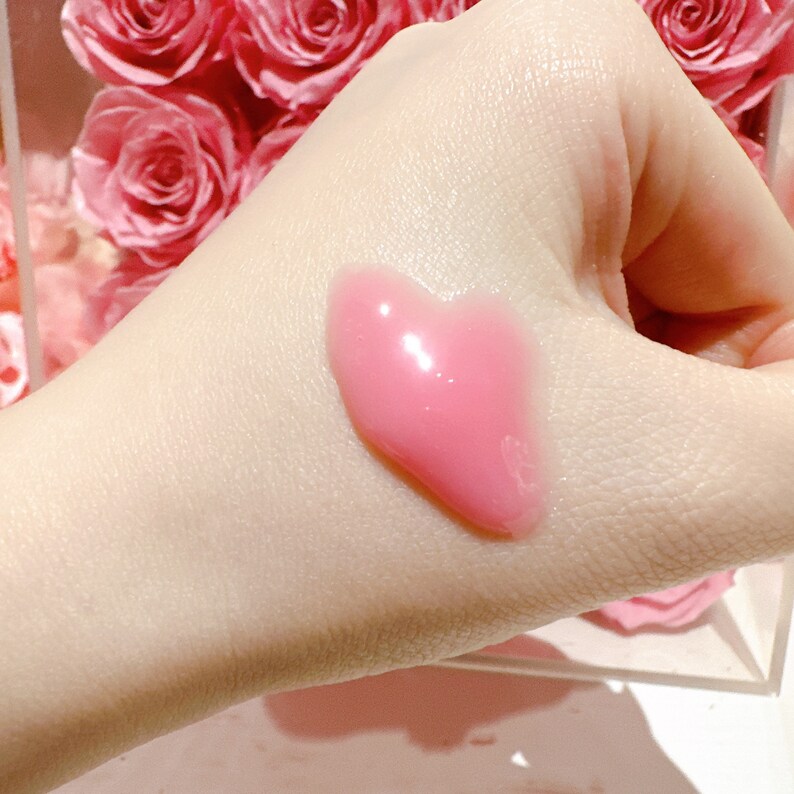 K&ouml;nnte beinhalten: Ein rosa herzf&ouml;rmiger Lippenbalsam oder Lipgloss auf der Hand einer Person.