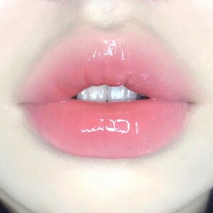 K&ouml;nnte beinhalten: Nahaufnahme von rosa Lippen mit gl&auml;nzendem Finish. Die Lippen sind leicht ge&ouml;ffnet und zeigen eine Reihe wei&szlig;er Z&auml;hne.