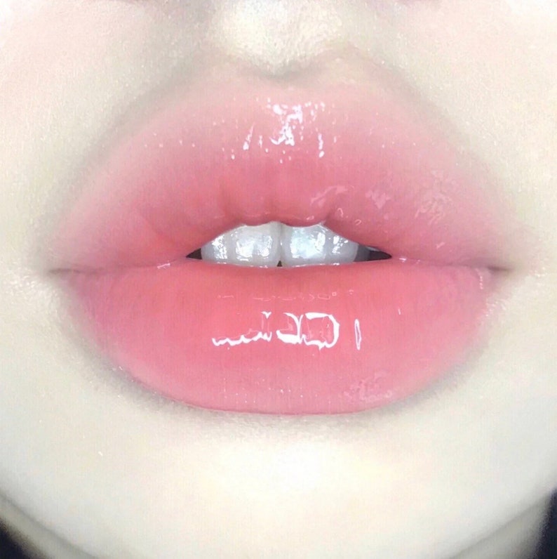 K&ouml;nnte beinhalten: Nahaufnahme von rosa Lippen mit gl&auml;nzendem Finish. Die Lippen sind leicht ge&ouml;ffnet und zeigen eine Reihe wei&szlig;er Z&auml;hne.