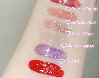 May include: Swatches of six different lip glosses on a person's arm. The colours are watermelon, grape, marshmallow, rose wine, bubble gum, and cotton candy.