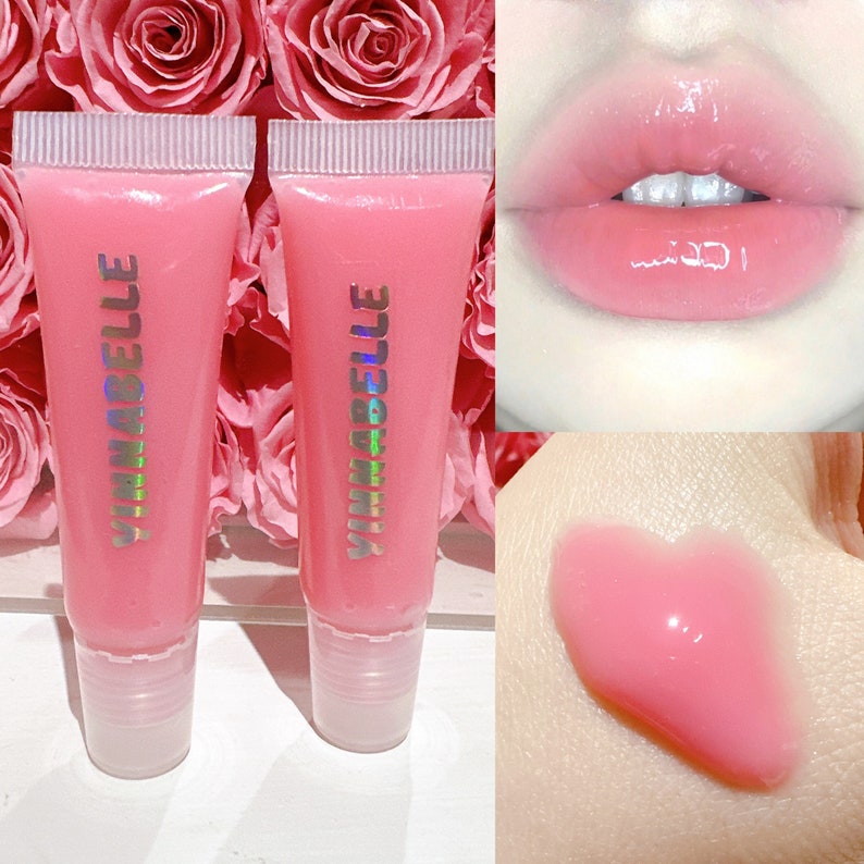 K&ouml;nnte beinhalten: Zwei rosa Lippenpflege-Tuben mit dem Aufdruck "YINABELLE" auf der Vorderseite. Der Lippenbalsam wird auf den Lippen einer Person und auf einer Hand gezeigt.