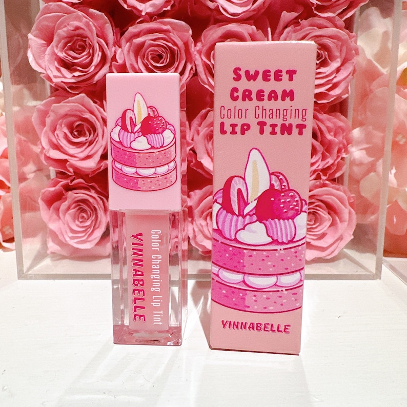 K&ouml;nnte beinhalten: Ein rosa und wei&szlig;es Lip Tint R&ouml;hrchen mit einem Kuchen-Design und dem Text "Sweet Cream Color Changing Lip Tint" und "Yinnabelle".