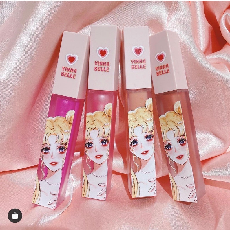 May include: Four clear lip gloss tubes with pink caps and a pink heart with the text "YINNA BELLE" on each tube. Each tube features a cartoon image of a blonde woman with a crown and a blue ribbon in her hair.